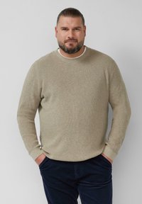 Beigefarbenes Strickpullover mit rundem Halsausschnitt, strukturiertem Stoff und langenÄrmeln, kombiniert mit dunkelblauen Hosen. Lässige, bequeme Passform.