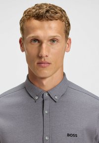 Camicia a maniche corte con bottone in modello pied de poule bianco e nero. Presenta un colletto button-down e un logo ricamato sul petto.