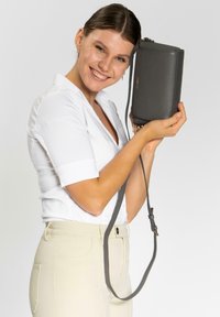 Borsa a tracolla grigia in pelle con superficie testurizzata e tracolla rimovibile. Presenta un logo impresso e un design minimalista. Forma rettangolare compatta.