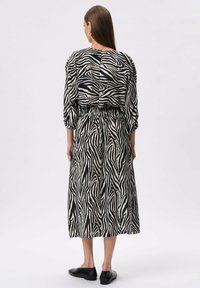 Sukienka w czarno-białe pasy zebry z dopasowaną talią, długimi rękawami i spódnicą o długości midi. Gładka tekstura materiału, luźny krój.