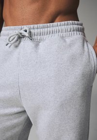 Graue Sweatpants aus weichem Material, mit einem elastischen Bund und einer Kordel, seitlichen Taschen und einer leicht strukturierten Oberfläche.