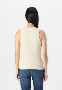 Beige ripstop tank topp med rund halsutringning, med brede skulderstropper og en tettsittende design. Kombinert med blå denimjeans.