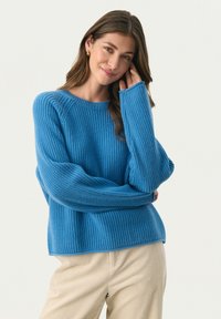 Lys blå ribbet sweater med rund halsudskæring og lange ærmer, der har en afslappet pasform og tekstureret finish. Sættes sammen med beige bukser.