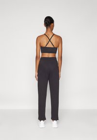 Zwarte sportbeha met kruisbanden, in combinatie met donkere joggingbroek met een relaxte pasvorm en geboorde randen, gedragen met witte sneakers.