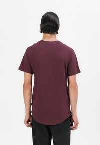 Camiseta de manga corta burdeos con cuello redondo y dobladillo curvado, hecha de una tela suave, que presenta un diseño simple y limpio.