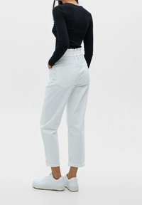 Weiße Jeans mit hohem, elastischem Bund, hochgekrempelten Säumen und Gesäßtaschen, kombiniert mit weißen Sneakers und einem schwarzen Langarmoberteil.