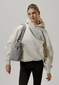 Felpa over-size color crema con tasca frontale, abbinata a una borsa grigia con coulisse. Tessuto morbido, vestibilità rilassata e polsini a costine. Leggings neri.