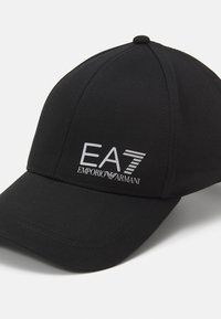 Fekete vászon baseball sapka, struktúrált formával. Elülső oldalán ezüst színű "EA7" és "Emporio Armani" logóval. Lapos karimával.