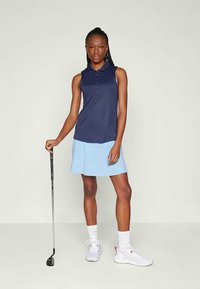 Sötétkék pólóing ujjatlan kivitelben, világoskék szoknyával párosítva. Az egyik kezében golfütőt tart, fehér sportcipő és zokni teszi teljessé a megjelenését.