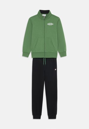 Žalias užtraukiamas megztinis su aukšta apykakle ir šoninėmis kišenėmis, derinamas su juodomis šniūreliais kelnių, turinčiomis mažą logotipą.