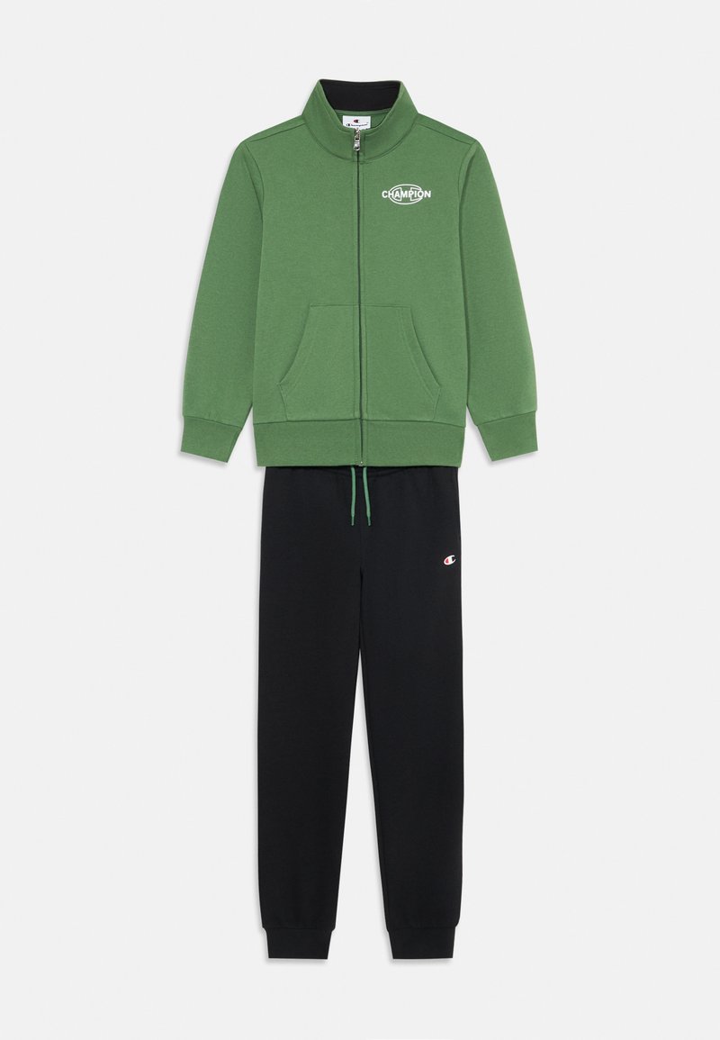 Sudadera verde con cremallera y cuello alto, combinada con pantalones de chándal negros con cordón y un pequeño logo.