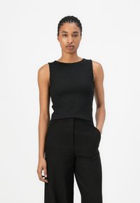 Zwarte mouwloze top met een gestructureerd patroon, ronde hals en aansluitende silhouet, gecombineerd met hoge zwarte broeken.