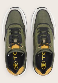 Sneaker verde oliva con accenti neri, tomaia texture e suola bianca. Presenta lacci neri e un logo giallo sulla linguetta.