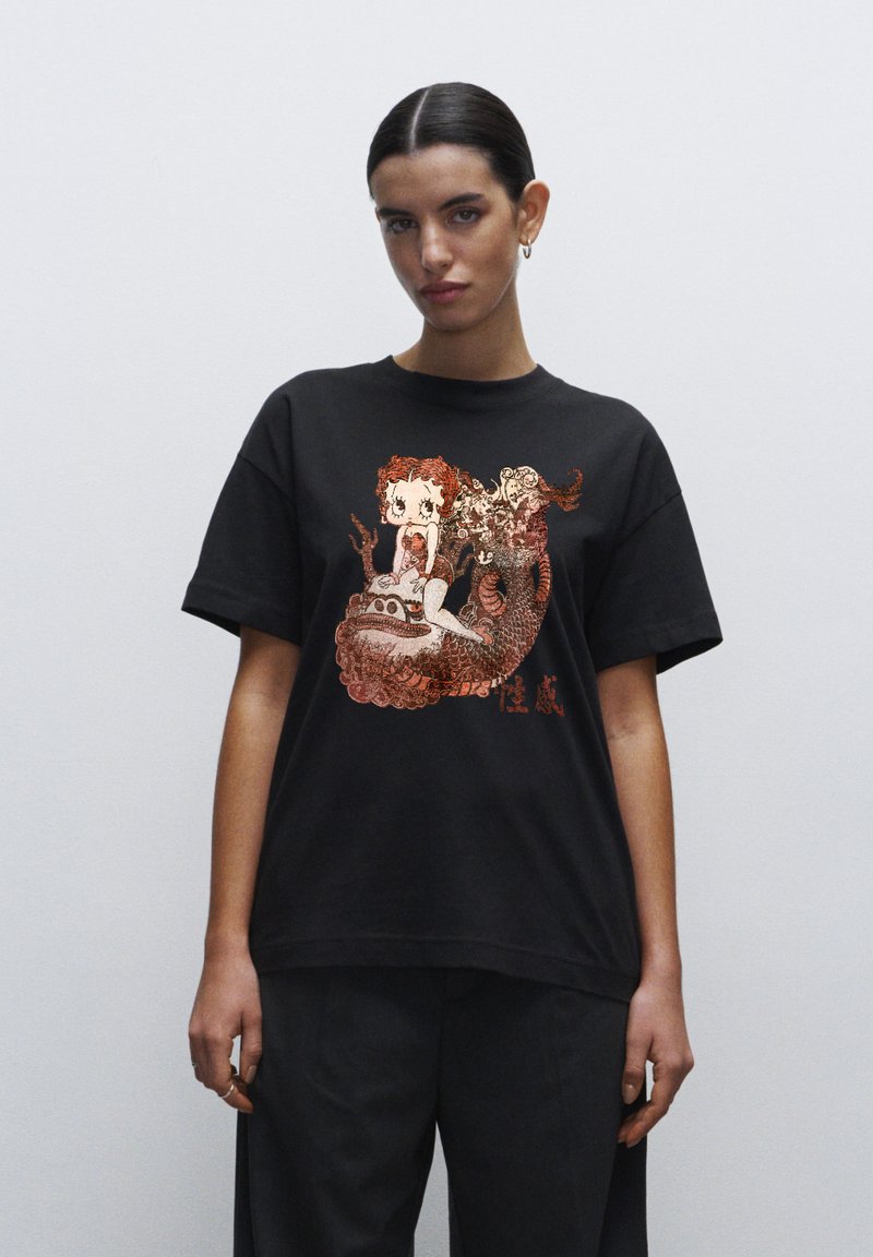 Camiseta negra de algodón, con un gráfico divertido en tonos rojos apagados y crema de un personaje con un fondo de dragón.