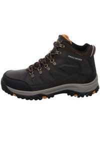 Bota de senderismo marrón con un upper texturizado, acentos naranjas y ojales de metal. Presenta una suela resistente con un dibujo prominente para una mejor tracción.