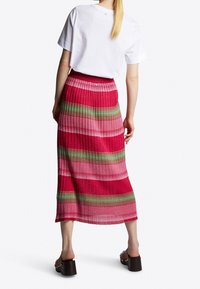 Rödrandig plisserad midi-kjol med gröna och rosa horisontella band; kombinerad med en vit t-shirt och svarta klacksandaler.