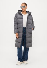 Giacca a vento grigia con cappuccio, design trapuntato, zip frontale e tasche laterali. Abbinata a una maglietta bianca, jeans larghi e sneakers.