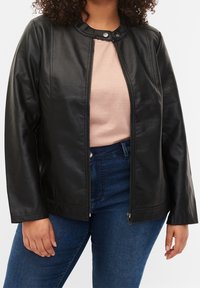 Veste en faux cuir noir avec col rond, fermeture éclair à l'avant et manches longues. Portée sur un haut rose clair et un jean bleu. Texture lisse.