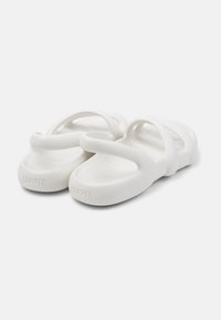 White rubber clogs with multiple curved straps and a smooth texture. Features an embossed logo on the heel. Lightweight design.
