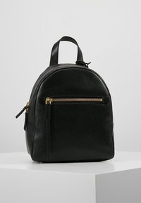 Schwarzer Leder-Rucksack in runder Form, mit Obergriff und vorderer Reißverschlusstasche. Mit goldenen Beschlägen und strukturiertem Oberflächenmaterial.