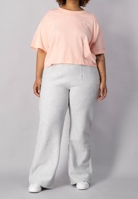 Lyserød cropped t-shirt med rund halsudskæring, parret med lysegrå, vide sweatpants. Outfittet har et afslappet og komfortabelt design.