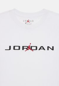 T-shirt bianco in cotone con scritta nera "JORDAN" e logo silhouette rosso, colletto rotondo e texture morbida.