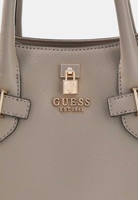 Szara torebka o fakturze z złotymi elementami metalowymi. Posiada wyraźne logo GUESS oraz ozdobne przeszycia na górnych i bocznych panelach.