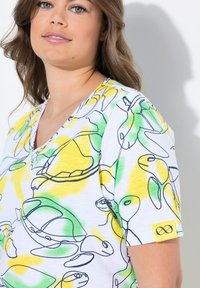 T-shirt a maniche corte di colore bianco con disegni di tartarughe in linea gialla e verde. Presenta un collo a V e un'etichetta gialla con un logo sulla manica.