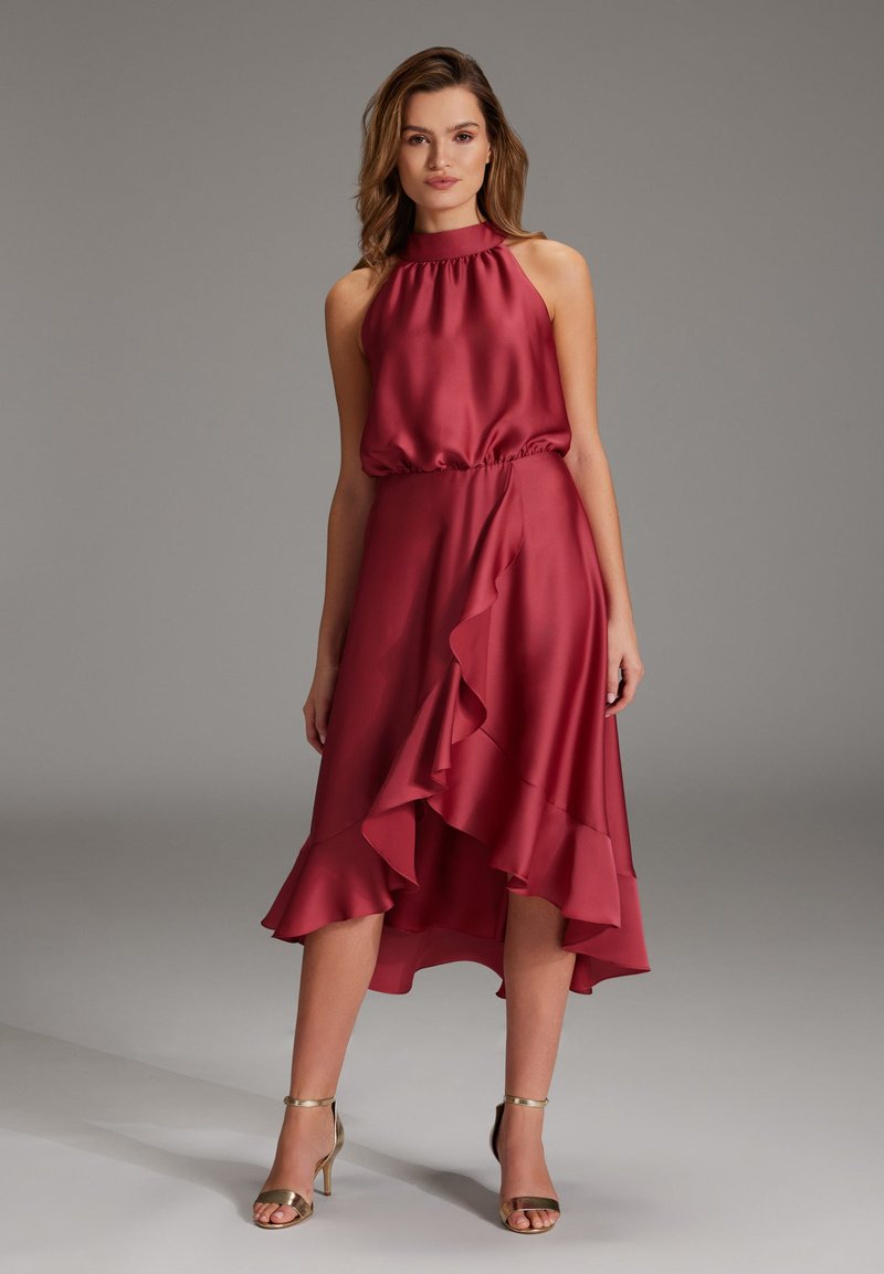 Robe en satin rouge avec un col montant, une taille élastique et un ourlet asymétrique à volants. Présente une texture lisse et une silhouette fluide.