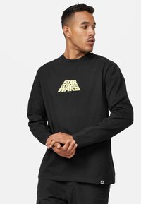 Svart långärmad t-shirt i bomull med en guld "STAR WARS"-logotyp på framsidan. Har rund halsringning och rak nederkant.