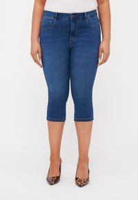 Mørkeblå denim caprijeans med middels høyde i livet, fem lommer og sømdetaljer, som har en tettsittende silhuett og hemmede ermer.