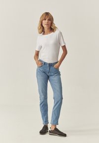 Tricou alb cu mânecă scurtă, asortat cu blugi de culoare albastru deschis și adidași negri. Blugii au o croială clasică, iar adidașii au un design minimalist.