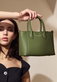 Grüne Lederhandtasche mit strukturiertem Finish, ausgestattet mit kurzen Griffen, goldenen Beschlägen und einem klaren Design. Markenlogo auf der Vorderseite sichtbar.
