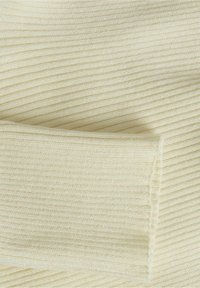 Krämfärgad ribbad stickad tyg som visar detaljerad textur och sömnad på en vikärm.