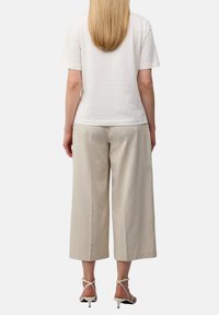 Witte katoenen t-shirt en beige wijde broek met een zachte textuur. De outfit wordt compleet gemaakt met witte sandalen met hakken en bandjes.