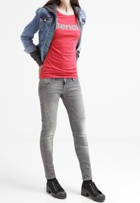 Chaqueta de mezclilla azul, camiseta gráfica roja, jeans grises con detalles texturizados y zapatillas de plataforma negras con cordones.