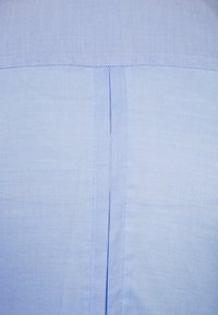 Ljusblått textil med en strukturerad yta, som har en vertikal söm och en subtil vävd mönster, vilket framhäver tygets struktur.