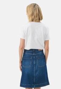 Jupe en denim A-line bleu moyen avec deux poches arrière, finition avec un ourlet cousu et portée avec un t-shirt blanc uni.