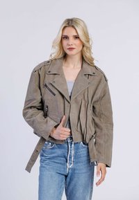 Grijze leren cropped jacket met asymmetrische ritsluiting, drukknoopjes en twee voorzakken met rits, gecombineerd met lichtblauwe spijkerbroek.