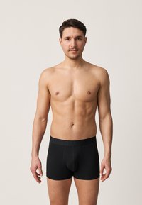 Schwarze Boxer-Shorts mit einem breiten elastischen Bund. Der Stoff wirkt glatt und dehnbar und verfügt über ein Design mit Vorderpouch.