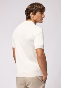 Polo shirt crema a maniche corte con colletto e orlo a coste, caratterizzato da una texture liscia e una vestibilità su misura, visto da dietro.