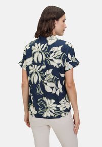 Navyblaues Kurzarmhemd mit einem weißen und grünen Blumenmuster, lockerer Passform und einer Rückenfalte.