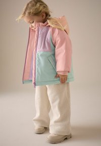 Färgglad puffjacka med mintgröna, rosa och lavendelfärgade paneler, med dragkedja och sidofickor, kombinerad med off-white strukturerade byxor och stövlar.