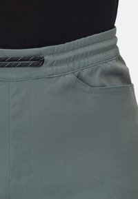 Lichtgroene joggers met een gladde textuur, voorzien van een zwarte trekkoordband en zijzakken. Eenvoudig, ontspannen ontwerp met gestikte details.