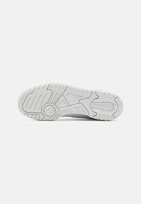 Weiße Sport-Schuhsohle mit texturiertem Gummiaufbau, versehen mit Rillen und kreisförmigen Akzenten, gekennzeichnet mit "new balance" Branding.