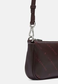Burgundowa skórzana torebka na ramię z srebnymi akcentami i zapięciem na zamek błyskawiczny, z dyskretnym wzorem wytłoczonym z nazwą marki.