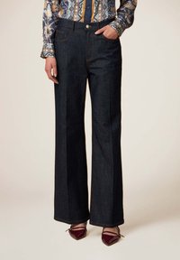 Pantalones de mezclilla de pierna ancha en azul oscuro con costuras naranjas, que cuentan con dos bolsillos frontales y un cierre de botón en la cintura.