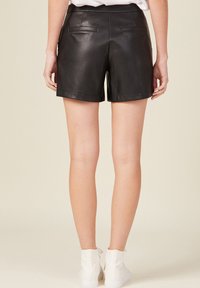 Pant shorts in pelle nera con un design sartoriale, dotati di due tasche posteriori e una texture liscia, che si fermano sopra la metà della coscia.