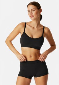 Musta bralette ja siihen sopivat shortsit, jotka on valmistettu pehmeästä ja joustavasta materiaalista. Mallissa on minimaalinen saumaus ja ohuet olkaimet.