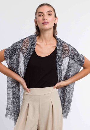 Kimono en imprimé léopard transparent en noir et blanc, tissu léger, design à ouverture frontale, porté par-dessus un débardeur noir et un pantalon taille haute beige.